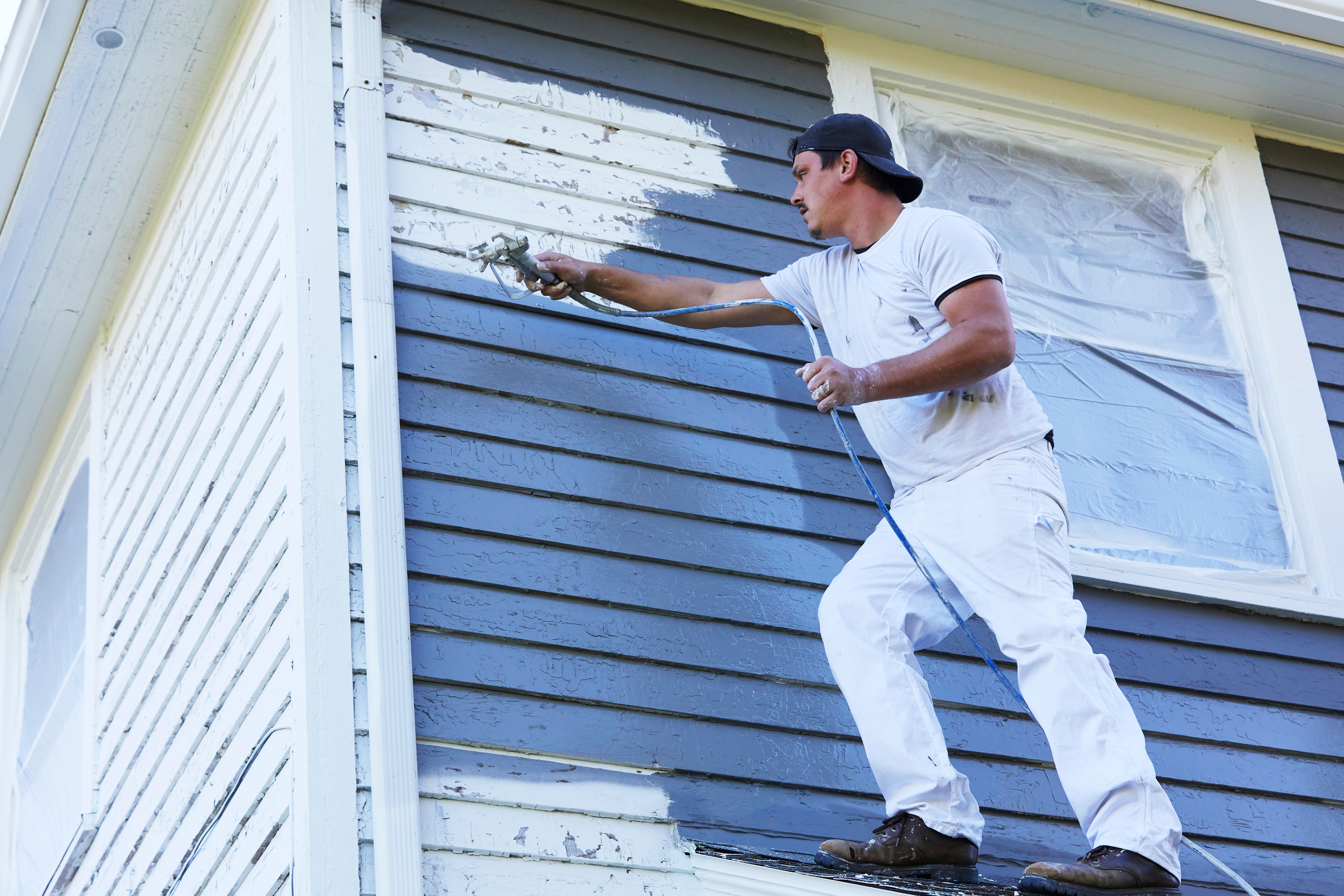 Man Spaying Paint On Exterior of Old House